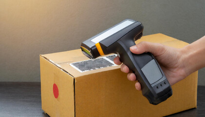 Close-up electronic portable barcode reader reads the barcode from the cardboard box, copy space. - obrazy, fototapety, plakaty