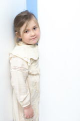Cute blond six-year-old little girl in pale party dress squeezing herself between two doors