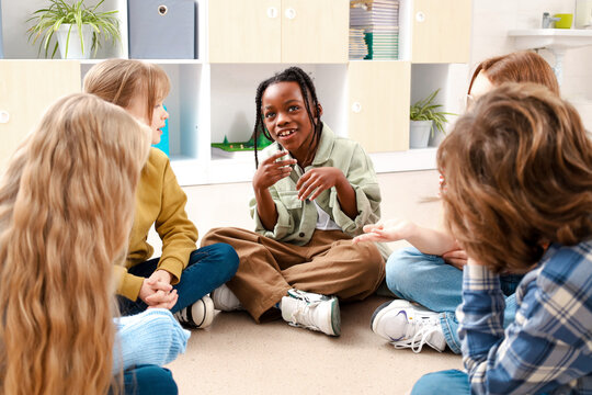 African American boy talking with his friends while sitting on the floor in classroom