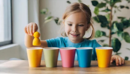 Foto op Plexiglas The girl learns colors by playing with wooden cylindrical toy colored human figures and placing them in cups of the appropriate color. The child is happy that he completed the task © richard