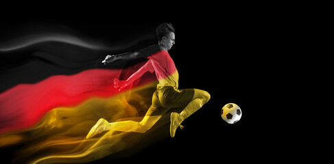 Concentrated young man, soccer athlete training, playing football on black background with flag of...