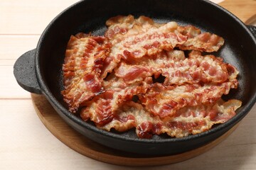 Delicious bacon slices in frying pan on white wooden table, closeup