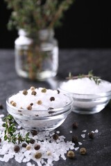 Salt with fresh thyme and peppercorns on dark grey textured table, closeup