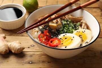 Bowl of delicious ramen and chopsticks on wooden table, closeup. Noodle soup