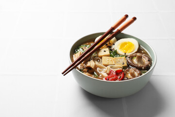 Noodle soup. Bowl of delicious ramen and chopsticks on white tiled table, space for text