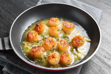 Delicious scallops with sauce in frying pan on dark gray textured table, closeup