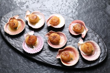 Delicious fried scallops in shells on black table