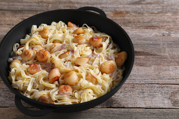 Delicious scallop pasta with onion in pan on wooden table, closeup