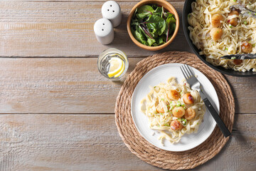 Delicious scallop pasta with onion served on wooden table, flat lay. Space for text