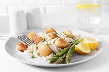 Delicious scallop pasta with asparagus, green onion and lemon served on white table, closeup