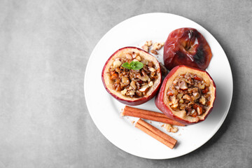 Tasty baked apples with nuts, honey, cinnamon sticks and mint on gray table, top view. Space for text
