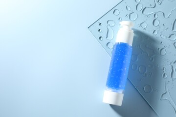 Bottle of cosmetic product on light blue background, top view. Space for text