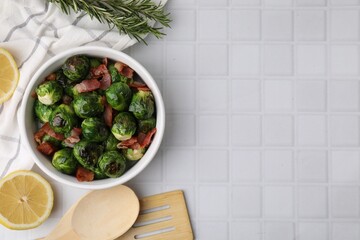 Delicious roasted Brussels sprouts and bacon served on white tiled table, flat lay. Space for text