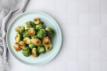 Delicious roasted Brussels sprouts on white tiled table, top view. Space for text