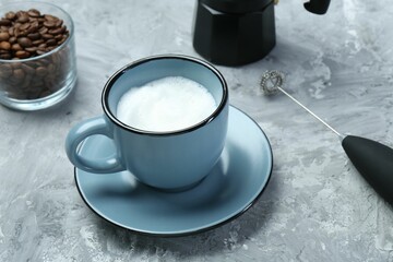 Mini mixer (milk frother), whipped milk in cup and coffee beans on grey textured table