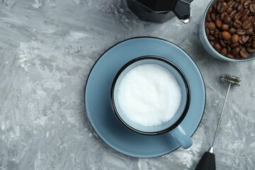 Mini mixer (milk frother), whipped milk in cup and coffee beans on grey textured table, flat lay....