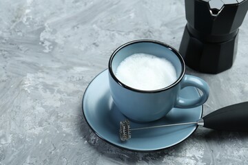 Obraz na płótnie Canvas Mini mixer (milk frother), whipped milk in cup and moka pot on grey textured table. Space for text