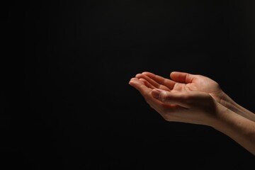 Religion. Woman with open palms praying on black background, closeup. Space for text