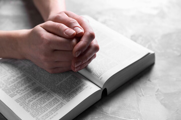 Religion. Christian woman praying over Bible at gray textured table, closeup