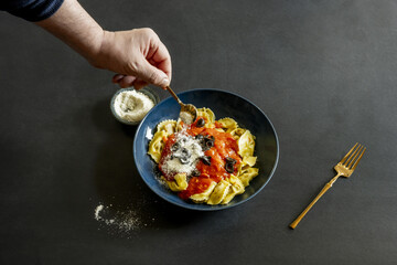 Photographing a man's hand sprinkling grated cheese on Italian pasta with tomato on a black surface second model