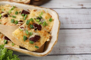 Taking piece of tasty sausage casserole from baking dish at white wooden table, closeup. Space for text