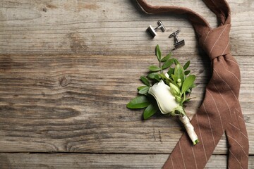 Wedding stuff. Stylish boutonniere, cufflinks and tie on wooden table, flat lay. Space for text
