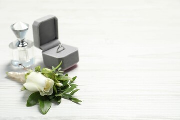 Fototapeta na wymiar Wedding stuff. Stylish boutonniere, perfume and ring on white wooden table, closeup. Space for text