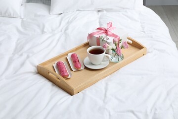 Fototapeta na wymiar Tasty breakfast served in bed. Delicious eclairs, tea, gift box, flowers and card with phrase I Love You on tray