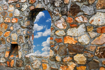 Blick durch ein Fenster einer historischen Mauer in den Wolkenhimmel