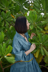 Woman touches the leaves of a lush plant, clothed in a casual blue dress, surrounded by vibrant greenery