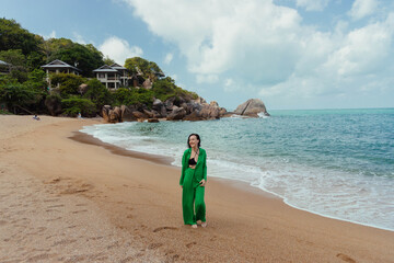 Woman enjoys a serene moment on a tropical beach with a luxurious villa nestled among boulders behind her