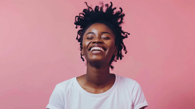 A smiling young Black woman, wearing a blank white t-shirt, poses against a pastel pink background in a studio shot 