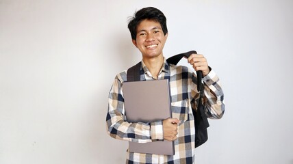 happy young asian male student carrying bag and holding laptop on isolated white background