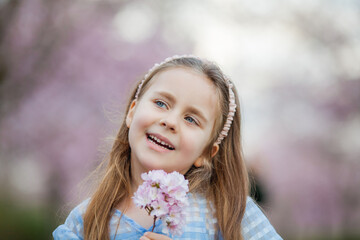 Cute smiling girl is walking along the street of cherry blossoms. Happy children. Warm bright...
