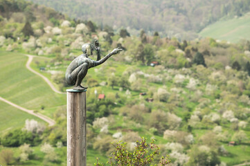 Weinberg mit Skulptur hockender Mann deutet in die Ferne
