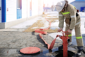 Image of a firefighter connecting a red fire hose to a hydrant for emergency water supply