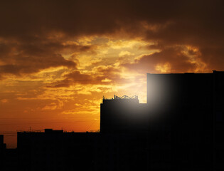 Dramatic sun flare above silhouettes of evening buildings - 780680022