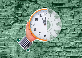 Composite Collage. Against the background of an old, weathered brick wall of pale green color, a man’s hand holds a large round clock showing the time at five minutes to twelve