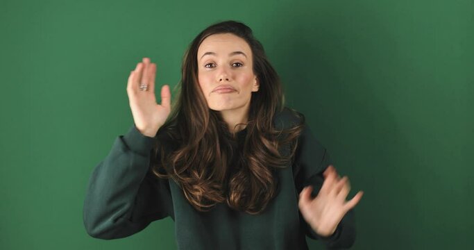 Thoughtful confused girl in green sweatshirt scratching head while thinking over solution, having doubts about difficult choice isolated on green background, not know, unsure, raised hands.