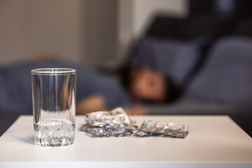 An empty glass and many packs of used empty pills on a table in the bedroom, blurred background....