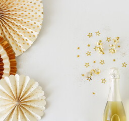 Birthday background top view with champagne bottle, golden stars decoration  and paper decor on white backdrop. Copy space. Holiday, party, wedding background.