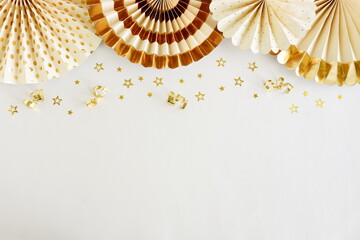 Birthday background template mock up  top view with golden fan paper decor and gold stars confetti on white backdrop. Copy space. Holiday, wedding, party background.