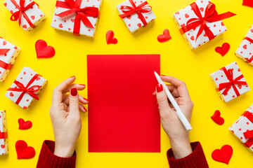 top view photo of valentine day decor female hands holding letter with envelope, small gift box and heart decoration on isolated pastel colored background with empty space