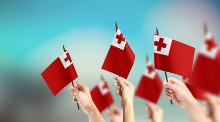 A group of people are holding small flags of Tonga in their hands.