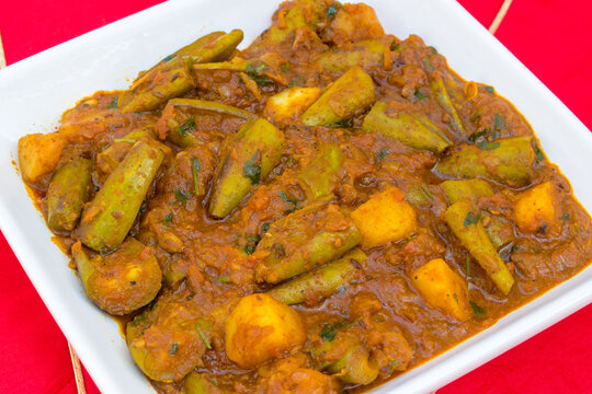 Indian Pointed Gourd Curry . Aloo Parwal Sabzi in white plate with red background