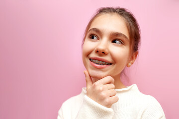 modest pensive teenage girl with braces thinks and imagines on a pink isolated background, the child is shy and plans and dreams - obrazy, fototapety, plakaty