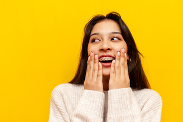 young modest asian girl with braces smiling and taunting on yellow isolated background, korean girl...