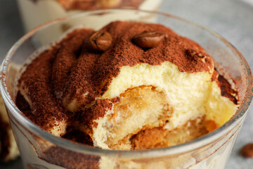 Delicious tiramisu in glass and coffee beans on table, closeup