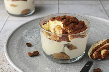 Delicious tiramisu in glass, coffee beans and spoon on table, closeup