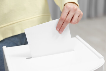 Woman putting her vote into ballot box on blurred background, closeup